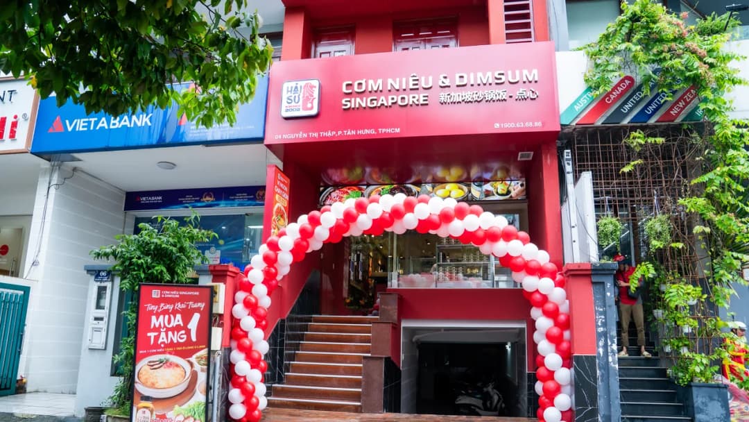 Mặt tiền nhà hàng Cơm Niêu Hải Sư: tấm biển đỏ trên cao ghi tên nhà hàng, logo, dòng địa chỉ và số điện thoại nhỏ ở mép dưới.