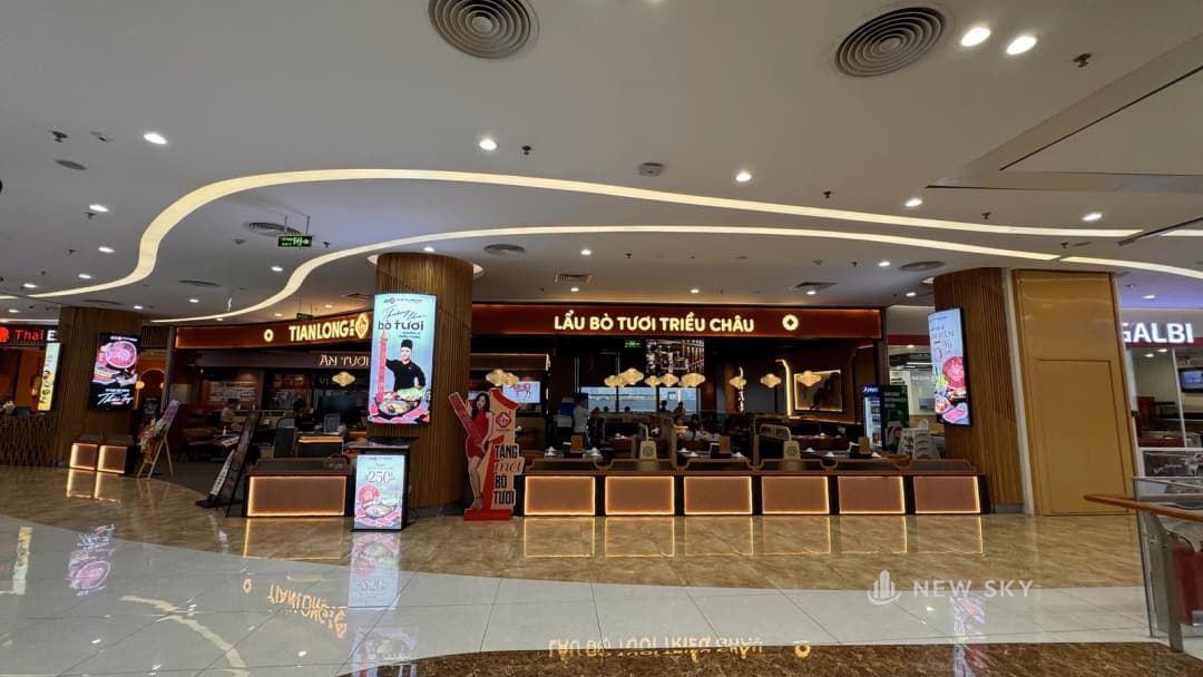 Mặt tiền một cơ sở Tian Long trong trung tâm thương mại Vincom Mega Mall Ocean Park lúc đang mở cửa: biển hiệu và dãy đèn hắt dưới quầy bật sáng, trần có cửa gió tròn và đèn âm, khách ngồi trong khu bàn phía sau.