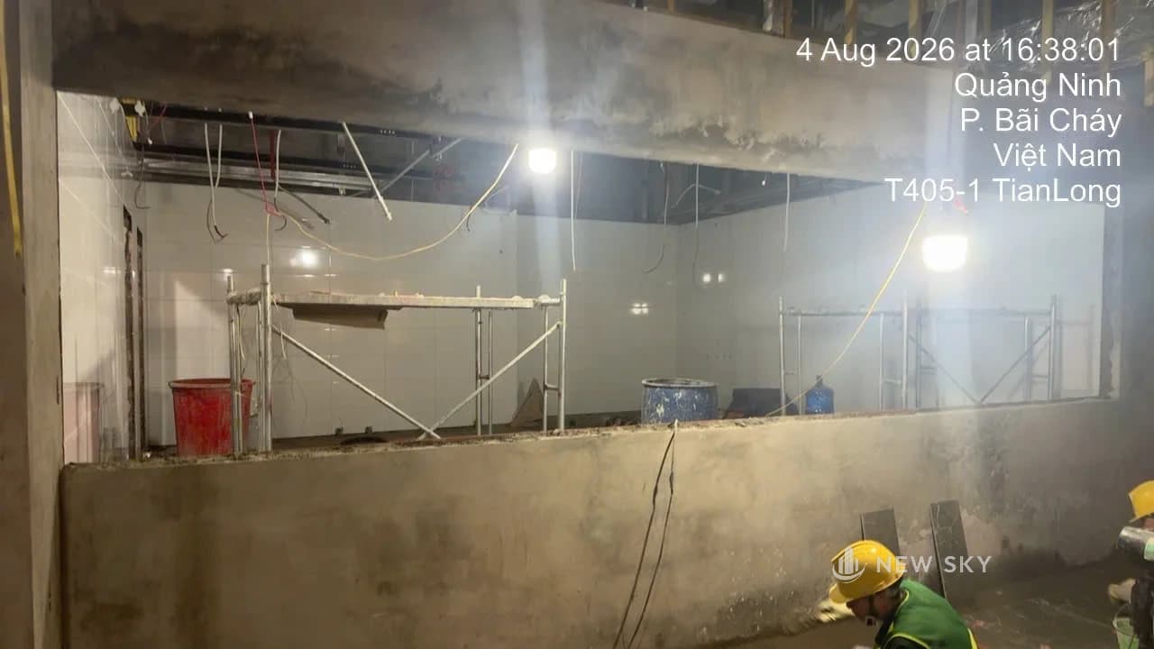 Thợ đội mũ bảo hộ làm trong mặt bằng nhà hàng đang thi công: tường đã ốp gạch trắng, giàn giáo dựng giữa phòng, dây điện còn thả từ trần.
