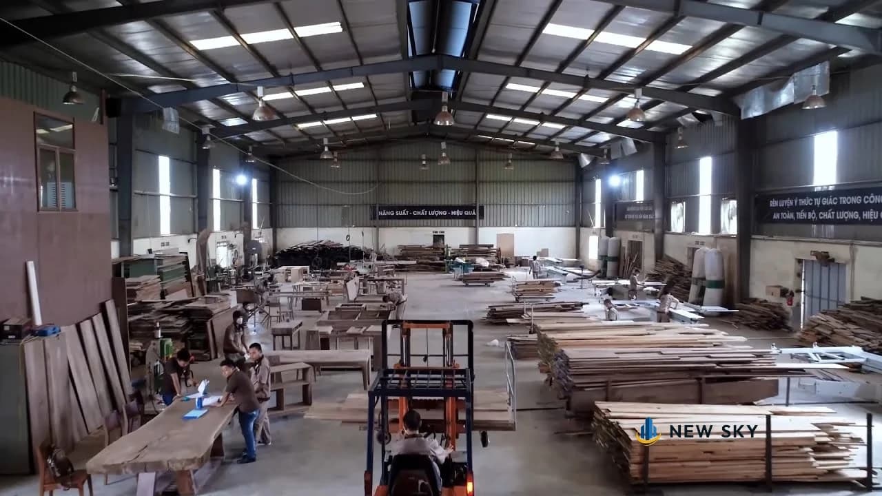 Dây chuyền nội thất trong xưởng Thượng Hồng nhìn từ trên cao: thợ đứng làm ở các bàn máy, gỗ xẻ xếp thành khối cao bên phải, một xe nâng tay ở lối đi giữa