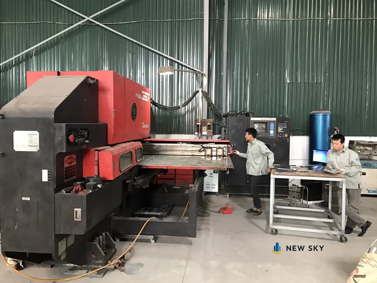 Hai thợ đứng máy đột dập tấm kim loại trong xưởng sản xuất của New Sky