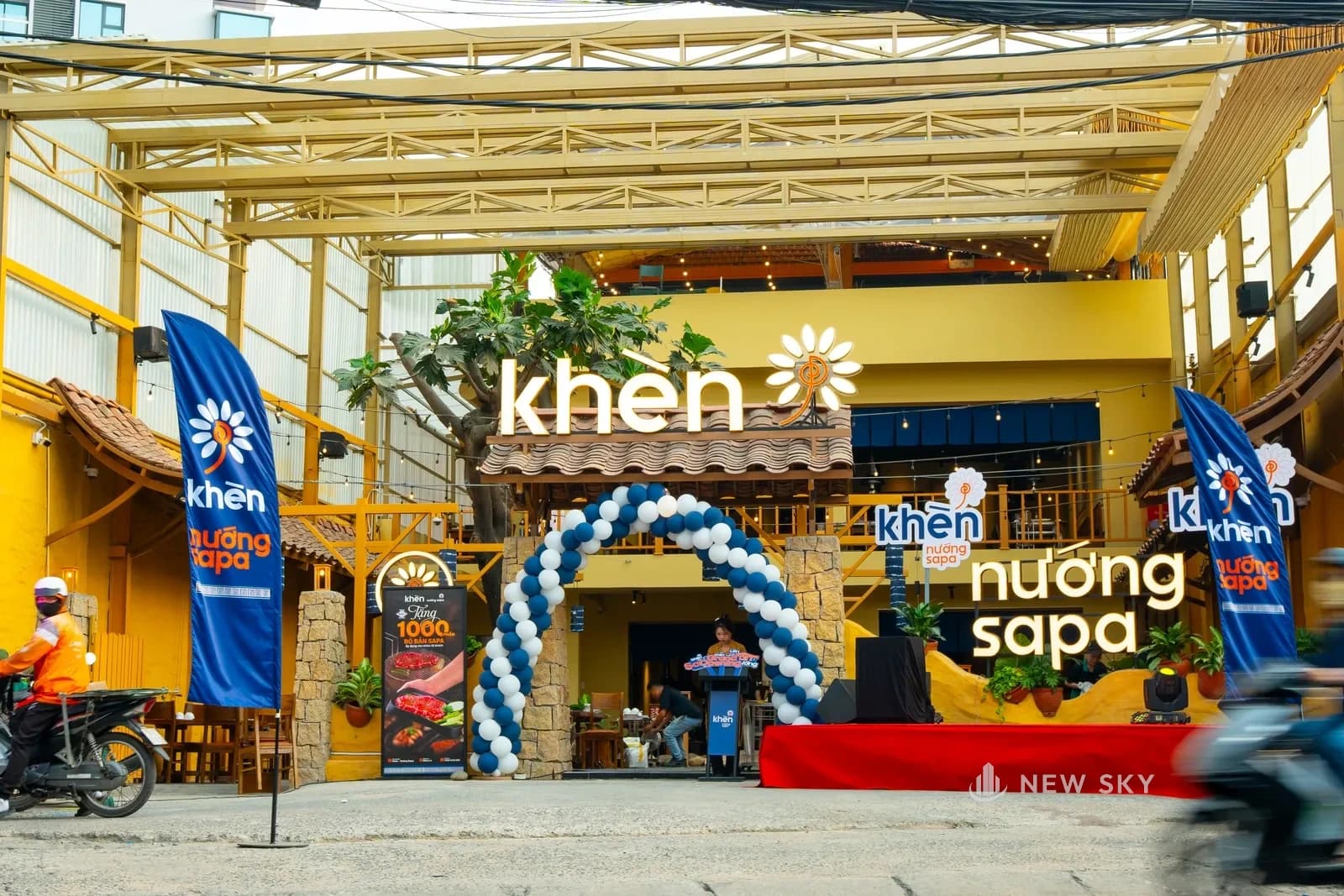 Mặt tiền Khèn Nướng Sapa 9 Thoại Ngọc Hầu ngày khai trương: biển chữ nổi tên nhà hàng gắn trên mảng tường vàng, một mái ngói nhỏ đỡ ngay dưới hàng chữ, khung giàn gỗ sơn vàng vươn ra che khoảng sân trước.