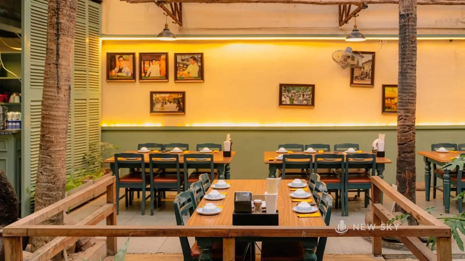 Phòng ăn có bàn gỗ dài, ghế gỗ, tường treo tranh nhỏ và đèn thả từ trần xuống mặt bàn.