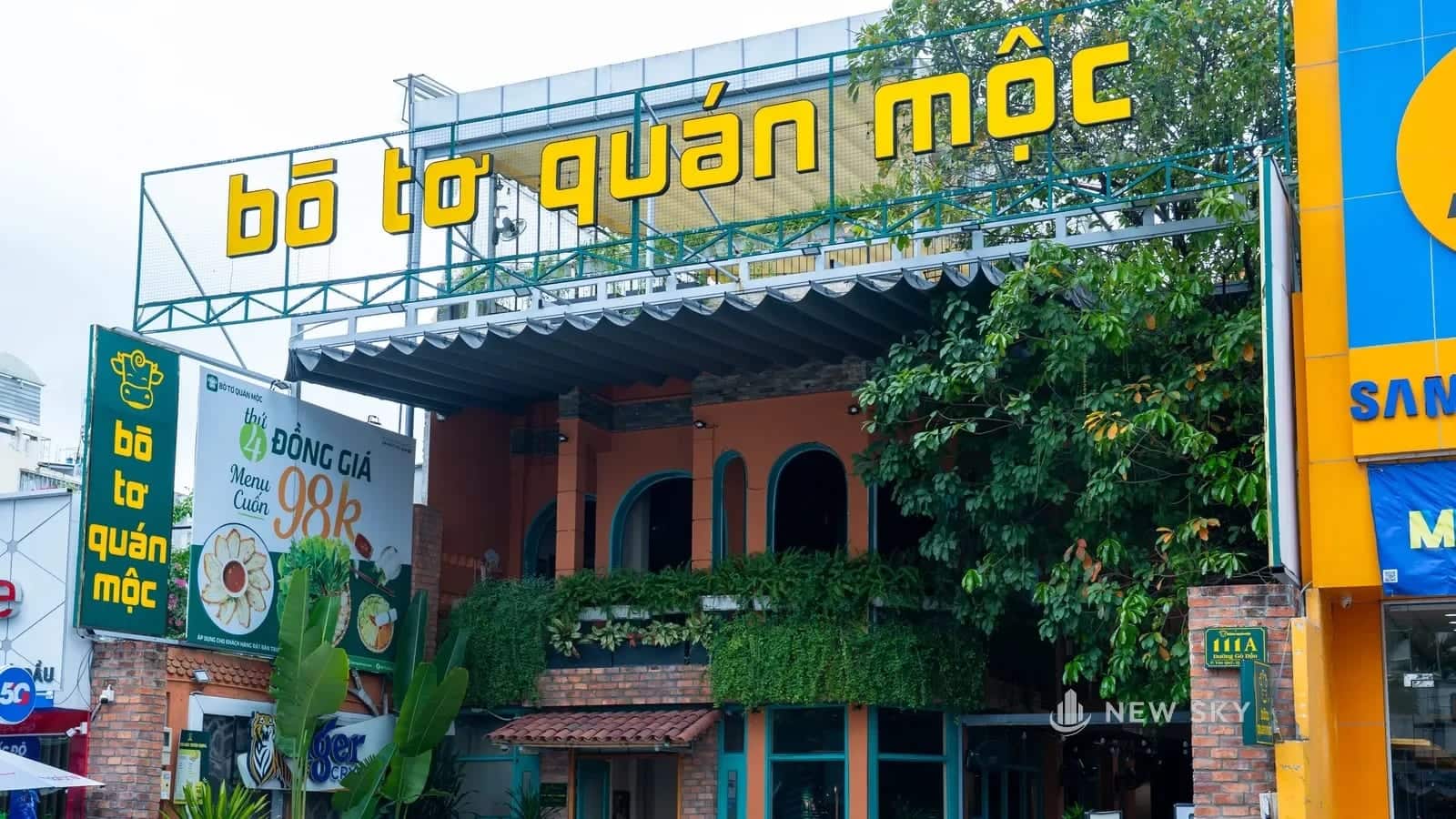 Biển hiệu ngang khổ lớn của nhà hàng Bò Tơ Quán Mộc số 111 Gò Dầu, gác trên khung thép riêng cao hơn mái, chạy suốt bề ngang mặt tiền.