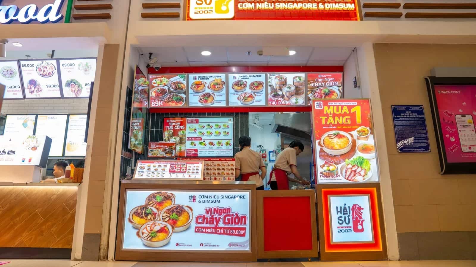 Quầy ki-ốt của một thương hiệu cơm niêu trong khu ẩm thực, nhân viên làm việc trong khu bếp hẹp phía sau quầy