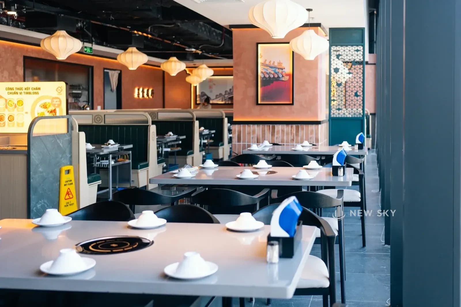Nhìn dọc gian ăn Tian Long Vincom Plaza Hồng Bàng: dãy bàn chạy sâu vào trong, tường hồng đất treo tranh khung, đèn lồng vải thả thành hàng.