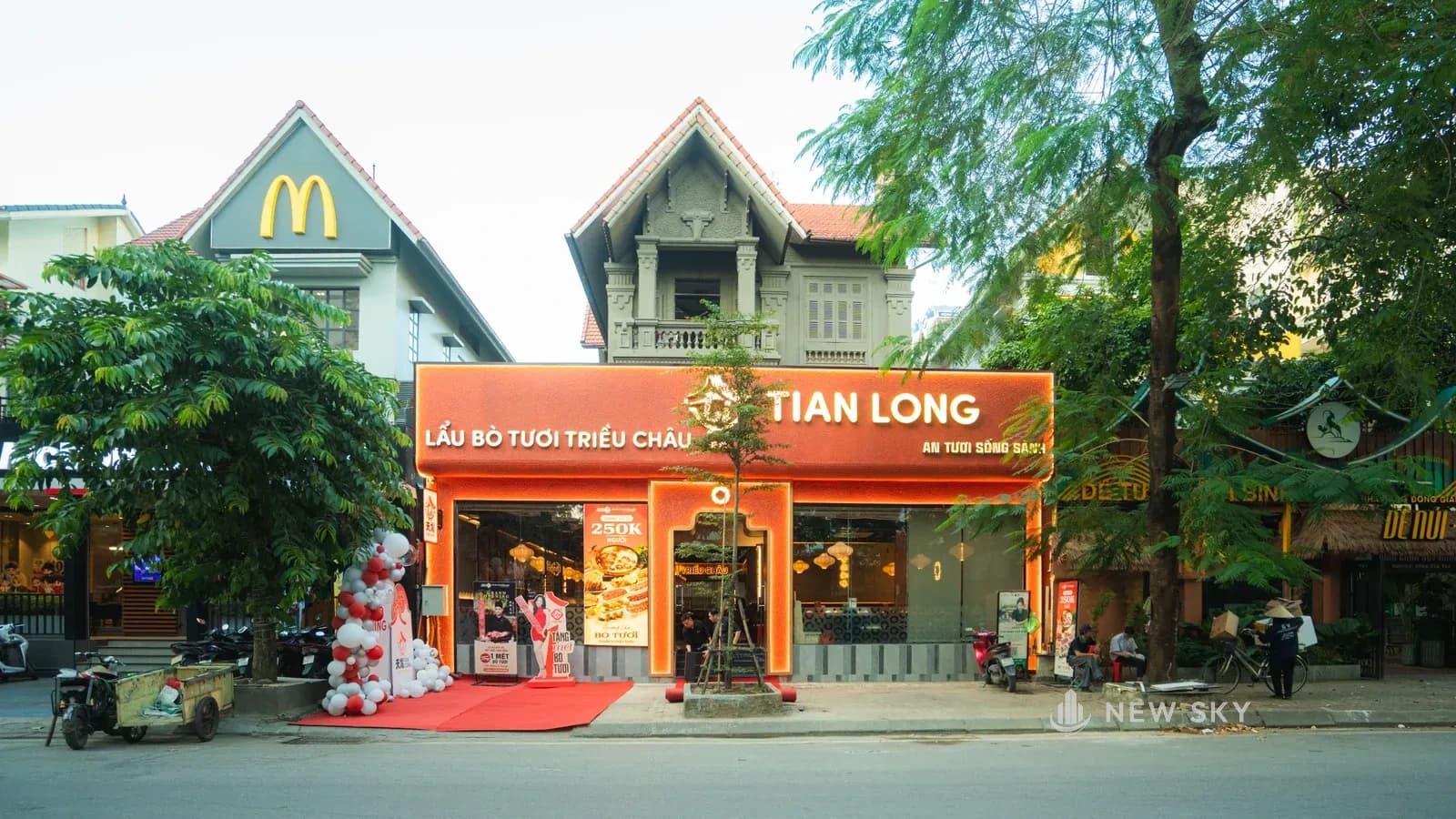 Mặt tiền nhà hàng Tian Long Linh Đàm, Hà Nội: biển hiệu cam chữ nổi, cổng vòm viền sáng, thảm đỏ và cụm bóng bay trước cửa.