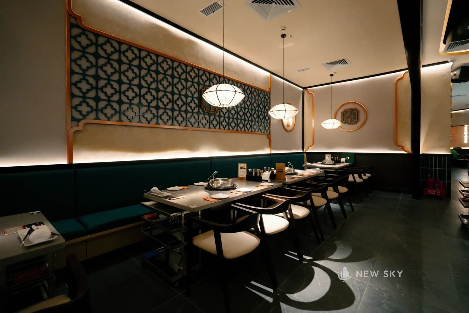 Phòng ăn Long Wang Vincom 191 Bà Triệu nhìn dọc: bàn kê thành hàng giữa nhà, ghế băng xanh ngọc bám tường, mảng hoa văn chữ thập xanh trên nền kem.