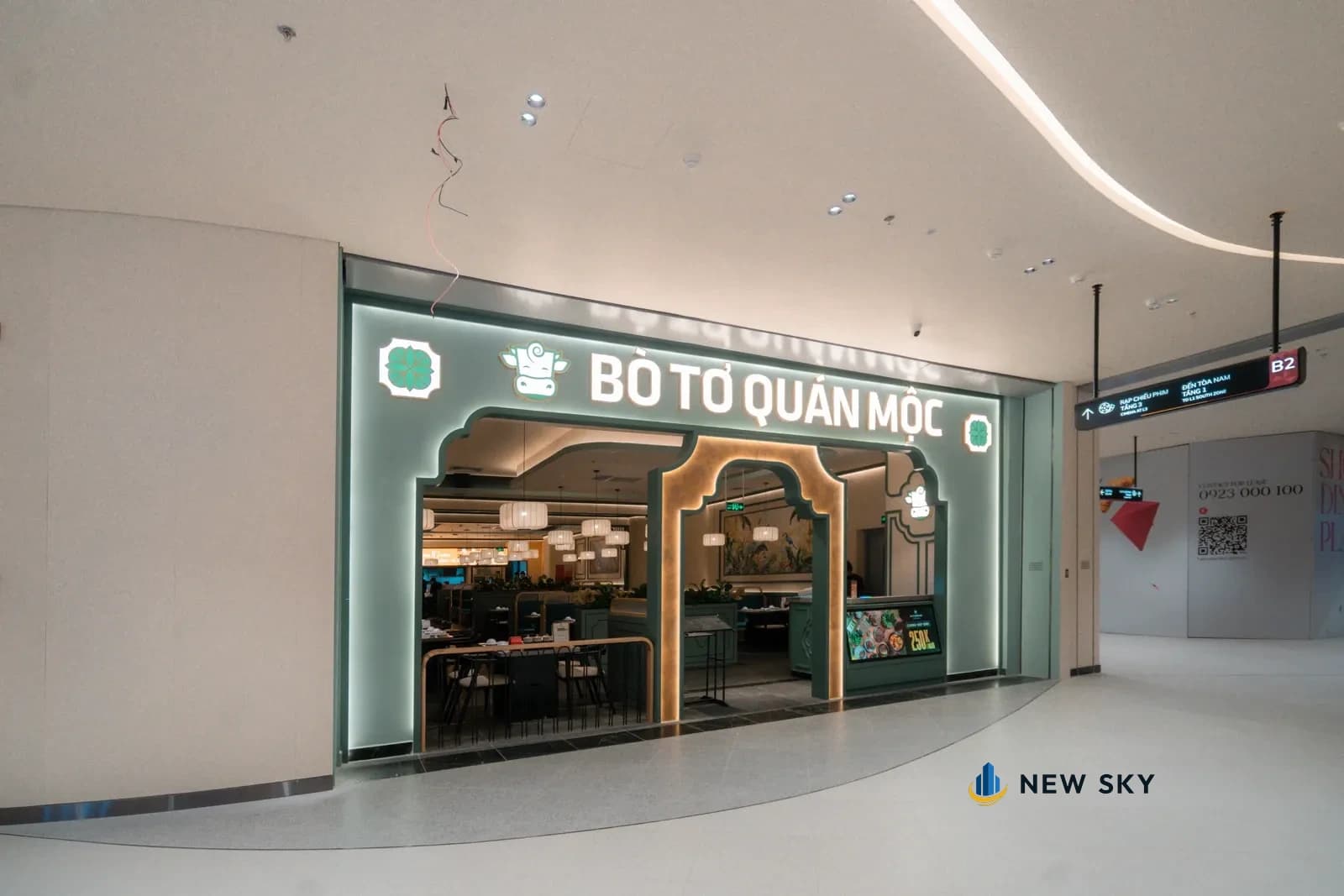 Cửa vào Bò Tơ Quán Mộc Hà Nội Center nhìn từ hành lang tầng B2: vách xanh cổ vịt, cửa khoét vòm viền kim loại vàng, chữ nổi phát sáng phía trên.