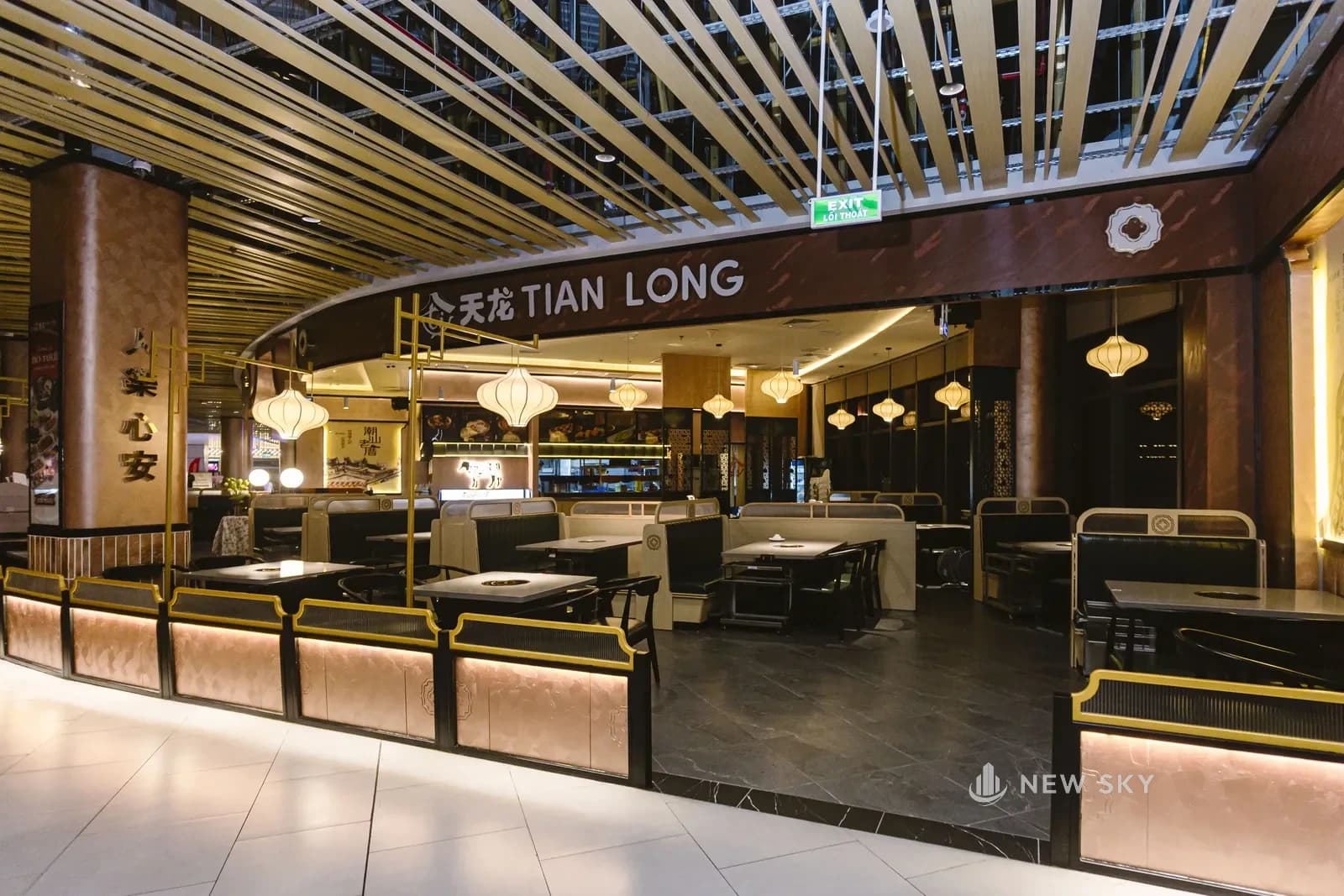 Mặt tiền Tian Long Aeon Mall Huế nhìn từ hành lang: biển hiệu chữ nổi trên vòm nâu, trần lam gỗ vàng chạy dọc, đèn lồng vải thả thành hàng phía trong.