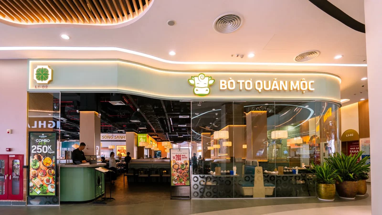 Mặt tiền Bò Tơ Quán Mộc ở tầng một Royal Island: biển nền kem chữ vàng, logo bò, mặt kính cong lượn theo dải trần.