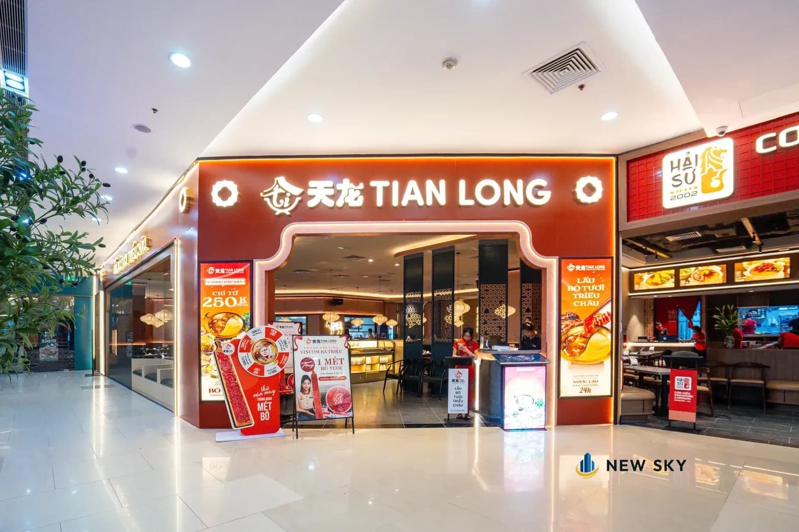 Cổng vòm Tian Long Vincom Bà Triệu nhìn từ hành lang: mảng tường màu đỏ cam quanh vòm, chữ 天龙 TIAN LONG trên đầu vòm, hai hộp đèn hai bên; bên phải là biển Hải Sư của nhà hàng bên cạnh.
