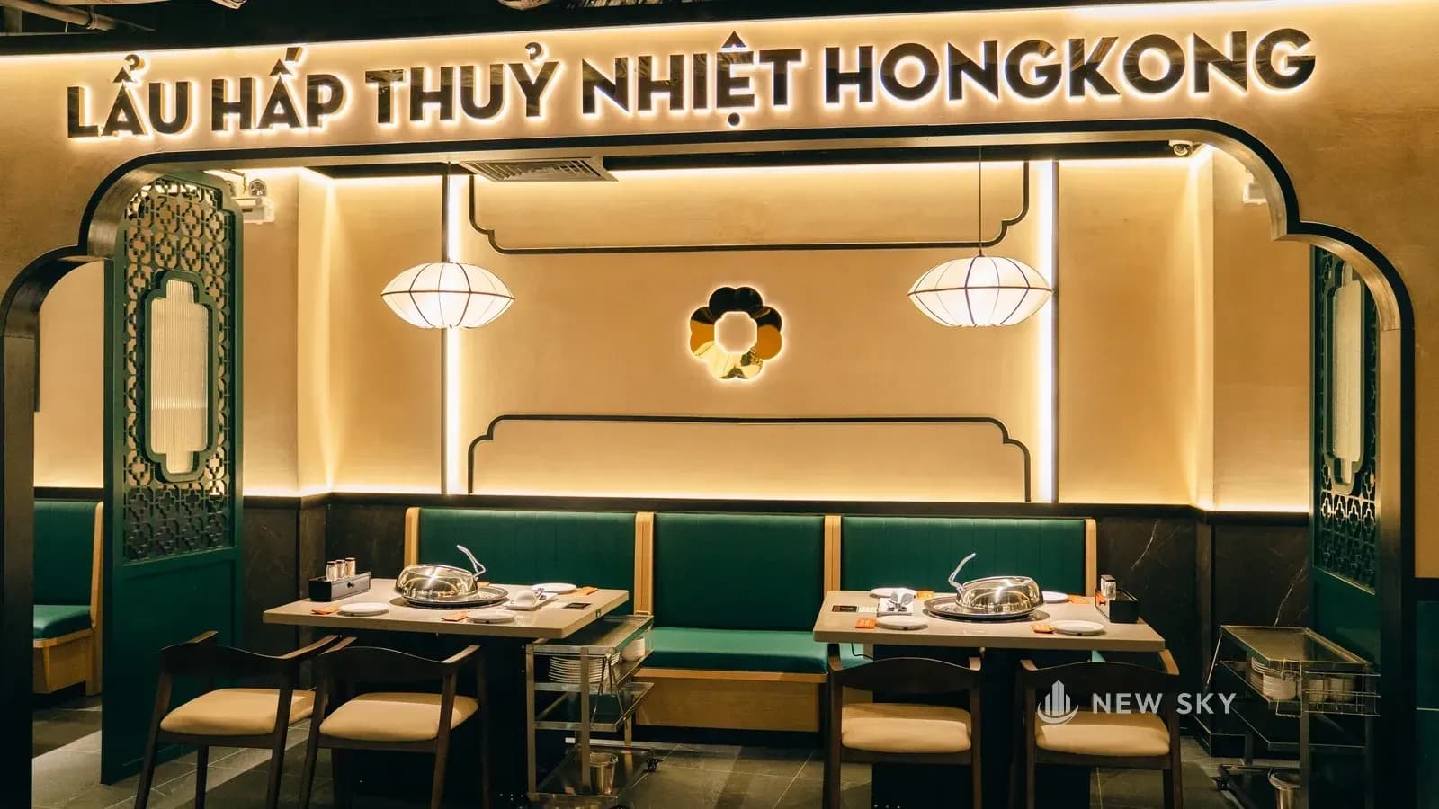 Một vòm nhìn gần: nét viền màu xanh sẫm, sát mép trong là khe hắt sáng chiếu lên mặt tường màu cát; bên dưới là băng ghế bọc da xanh rêu và bàn có nồi hấp.