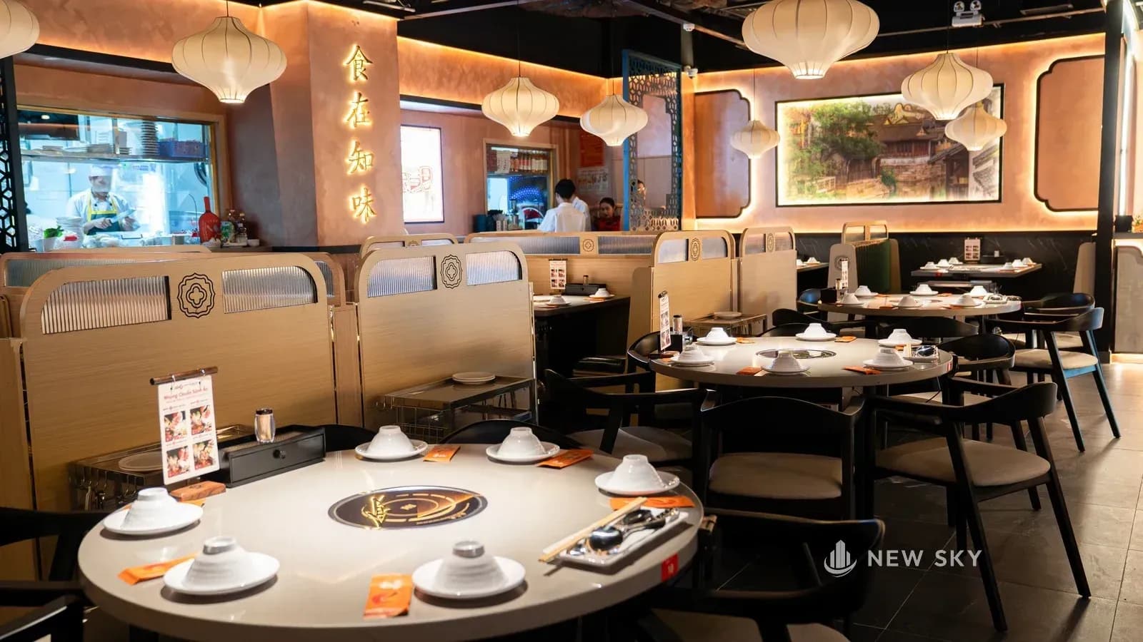 Ô mở thứ hai trên tường cuối gian nhìn vào bếp, bên cạnh là mấy chữ Hán gắn nổi màu vàng trên tường vữa cam đất; phía trước là bàn tròn và khoang ghế.