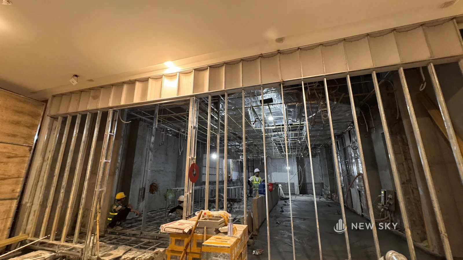 Mặt bằng thô của một nhà hàng trong Aeon Mall Hạ Long: khung vách thép đã dựng, trần chưa đóng nên lộ ống gió bọc bảo ôn và dây chờ thả xuống, mấy người thợ đội mũ bảo hộ đang làm bên trong.